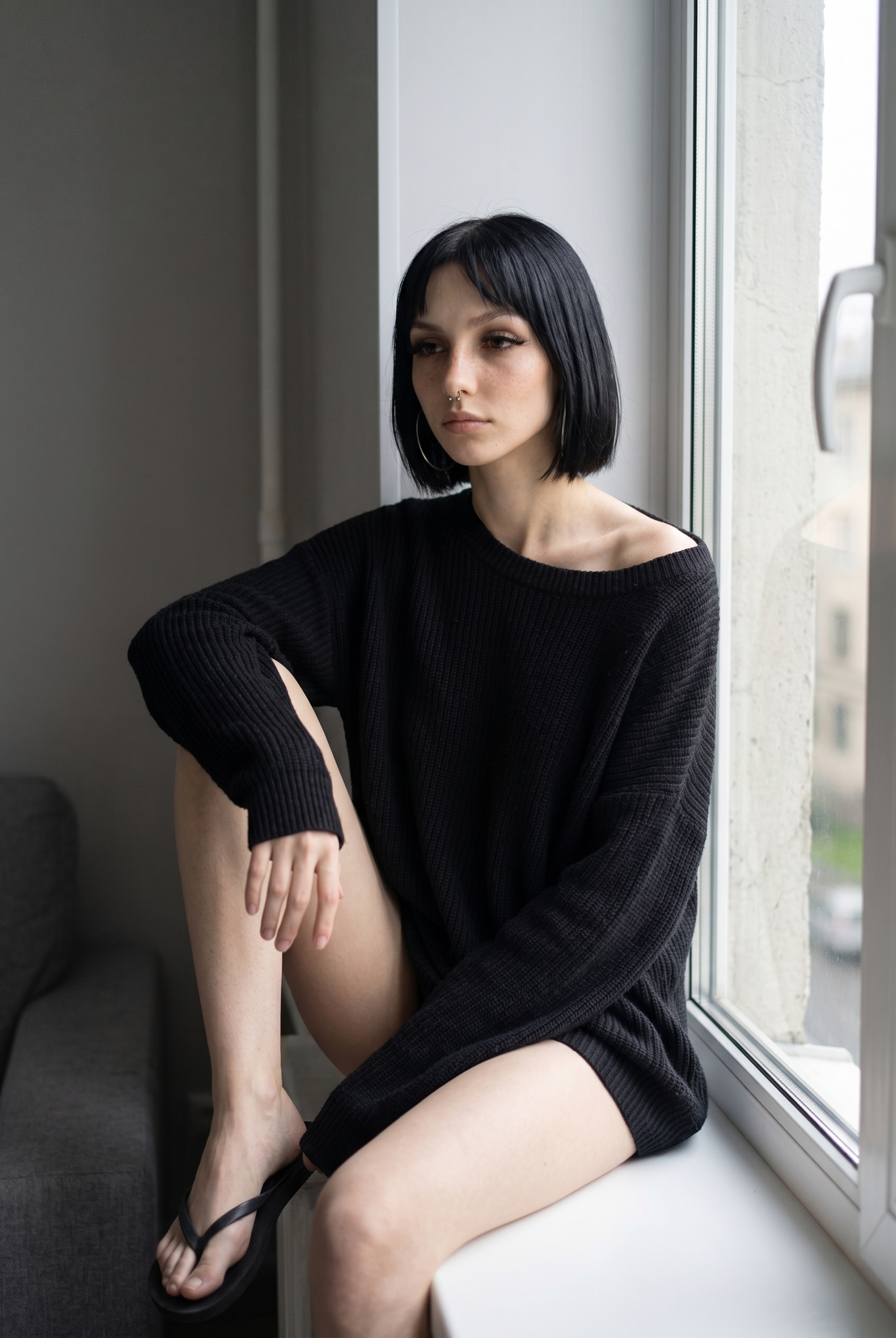 Gloria sitting by a window with one knee raised.